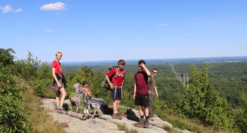 A group of students stand on a rocky overlook, high above the green terrain below. 
